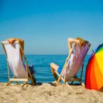 Urlauber sitzen auf Liegestühlen am Strand mit Blick auf das Meer