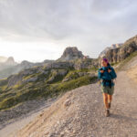 Wanderin mit Rucksack auf einem Bergpfad in den Dolomiten bei Sonnenuntergang.